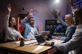 Four multiracial office colleagues sitting at the table with arms raised