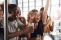 Group Of Male And Female Friends Celebrating Whilst Watching Game On Screen In Sports Bar