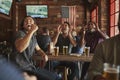 Group Of Male Friends Celebrating Whilst Watching Game On Screen In Sports Bar