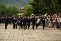 Group of male musicians in military uniforms playing large instruments, marching in a parade