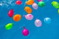 Group of many colorful plastic water balloons floating in the water of a pool to entertain their children on summer vacations Royalty Free Stock Photo