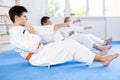 Group of men of different ages in white kimono train abdominal muscles and do punches at the same time during karate or