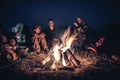 Group of people explorers resting by the fire in outdoors camp after long hiking day in the night
