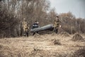 Group of men hunters in camouflage with rubber boat crossing dry rural field with bushes on background during spring hunting