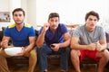 Group Of Men Sitting On Sofa Watching Sport Together