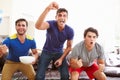 Group Of Men Sitting On Sofa Watching Sport Together