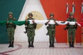 Group of military soldiers are standing in formation, each holding a Mexican flag