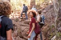 Group of millennial friends hiking uphill on a forest trail, three quarter length