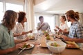 A group of millennial friends sitting at a table, eating lunch and talking, backlit