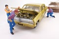 Miniature mechanics work on a gold toy car.