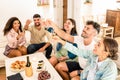 Group of mixed race friends toasting with champagne celebrating at home - Young multiracial people sitting on the sofa clinking Royalty Free Stock Photo