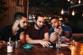 Group of mixed race young men talking and using phone in lounge bar. Multiracial friends having fun in cafe Royalty Free Stock Photo