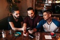 Group of mixed race young men using phone and talking in lounge bar. Multiracial friends having fun in cafe Royalty Free Stock Photo