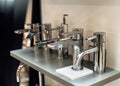 Group of modern stylish water taps for bathroom in showroom. Rows of new faucets in plumbing shop, closeup. Selective