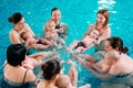 A group of mothers with their young children in a children`s swimming class with a coach.