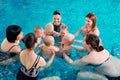 A group of mothers with their young children in a children`s swimming class with a coach.