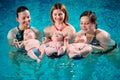 A group of mothers with their young children in a children`s swimming class with a coach.