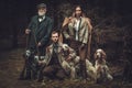 Group of multi-age hunters with dogs and shotguns in a traditional shooting clothing, posing on a dark forest background Royalty Free Stock Photo