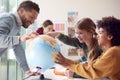 Group Of Multi-Cultural Students With Teachers In Classroom Looking At Globe In Geography Lesson