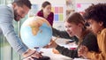 Group Of Multi-Cultural Students With Teachers In Classroom Looking At Globe In Geography Lesson