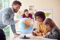 Group Of Multi-Cultural Students With Teachers In Classroom Looking At Globe In Geography Lesson