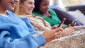 Group Of Multi-Cultural Teenage Girl Friends Snuggled Under Blanket Looking At Mobile Phones At Home Royalty Free Stock Photo