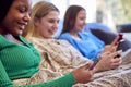 Group Of Multi-Cultural Teenage Girl Friends Snuggled Under Blanket Looking At Mobile Phones At Home Royalty Free Stock Photo