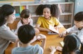 Group of Multi-ethnic happy elementary school and Female Asian teacher sitting on chairs in circle around with them and talking in Royalty Free Stock Photo