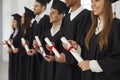 Group of multiethnic people standing in a row and holding scrolls of diplomas in their hands. Royalty Free Stock Photo