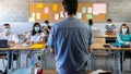 Group of multiracial teen high school students wearing face mask listen to teacher lesson. Rear view of teacher. Royalty Free Stock Photo