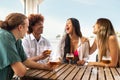 Group of multiracial young friends laughing, talking and having fun at beach bar drinking beers together. Royalty Free Stock Photo