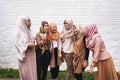 Group of Muslim Asian women wearing hijab standing and having conversation by white brick wall