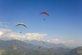 A group of paragliders on colored parachutes in a clear blue sky over a mountain valley