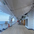 A group of passengers lounging in chairs under the life rafts on the deck of a cruise ship