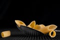 Group of penne macaroni pasta in a large chrome spoon on a black background