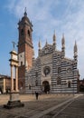 Group of people ambling past the towering Monza Cathedral on a sunny day. Italy.