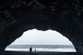 Group of people on the beach at sunset, standing under an old tunnel arch, Iceland Royalty Free Stock Photo