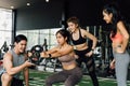 Group of people cheering on their Asian female friend doing squats with a weight plate in fitness gym. Working out Royalty Free Stock Photo