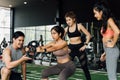 Group of people cheering on their Asian female friend doing squats with a weight plate in fitness gym. Working out Royalty Free Stock Photo