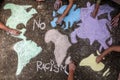 A group of people drawing with colored chalks on the floor a map of the world with words No Racism Royalty Free Stock Photo