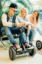 Group of people on electric scooter hoverboard sitting at bench and using phone Royalty Free Stock Photo
