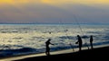 Group of people enjoying a leisurely afternoon of fishing off the beach at sunset