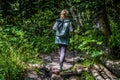 Group of people go hiking in wooded and hilly area. Rear view of woman engaged in nordic walking on rocky path. Royalty Free Stock Photo