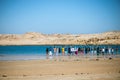 A group of people holding hands each other and standing near a blue lake surrounded by a desert