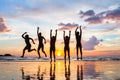 Group of people jumping on the beach at sunset, silhouettes of happy friends