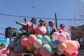 A group of people in pink shirts riding a float of balloons on the street Royalty Free Stock Photo