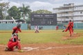 Group of people playing baseball on a green field with a scoreboard visible in the background