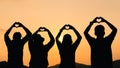 Group of people with raised arms and make hand to the heart shape looking at sunrise on the mountain background. Happiness, Royalty Free Stock Photo