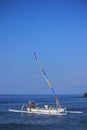 Group of people riding in a white Balinese fishing boat with a colorful sail.