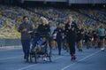 Group of people running on tracks of the stadium, woman running and pushing the wheelchair with disabled boy, cerebral palsy